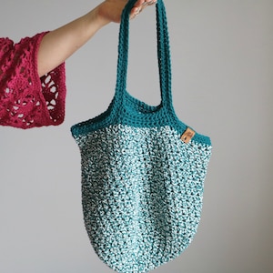 May include: A teal and white crocheted tote bag with a brown leather tag. The bag has a wide base and two long straps.
