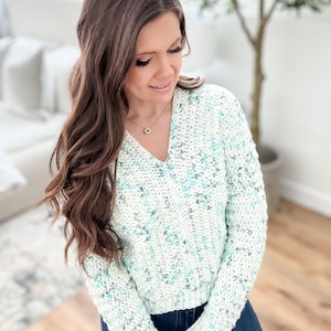 May include: A white and light blue crochet sweater with a v-neck and long sleeves.