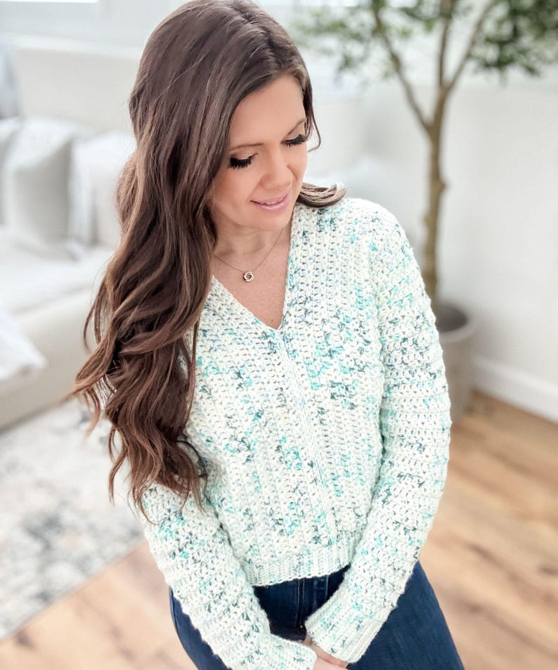May include: A white and light blue crochet sweater with a v-neck and long sleeves.