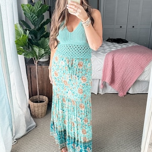 May include: A woman wearing a light blue crochet top and a long, flowing floral maxi skirt. The skirt has a tiered design and features a variety of floral patterns in shades of blue, green, and orange.
