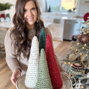 May include: Four crocheted Christmas trees in white, green, and red on a silver tray. The trees are cone-shaped and have a sparkly texture.