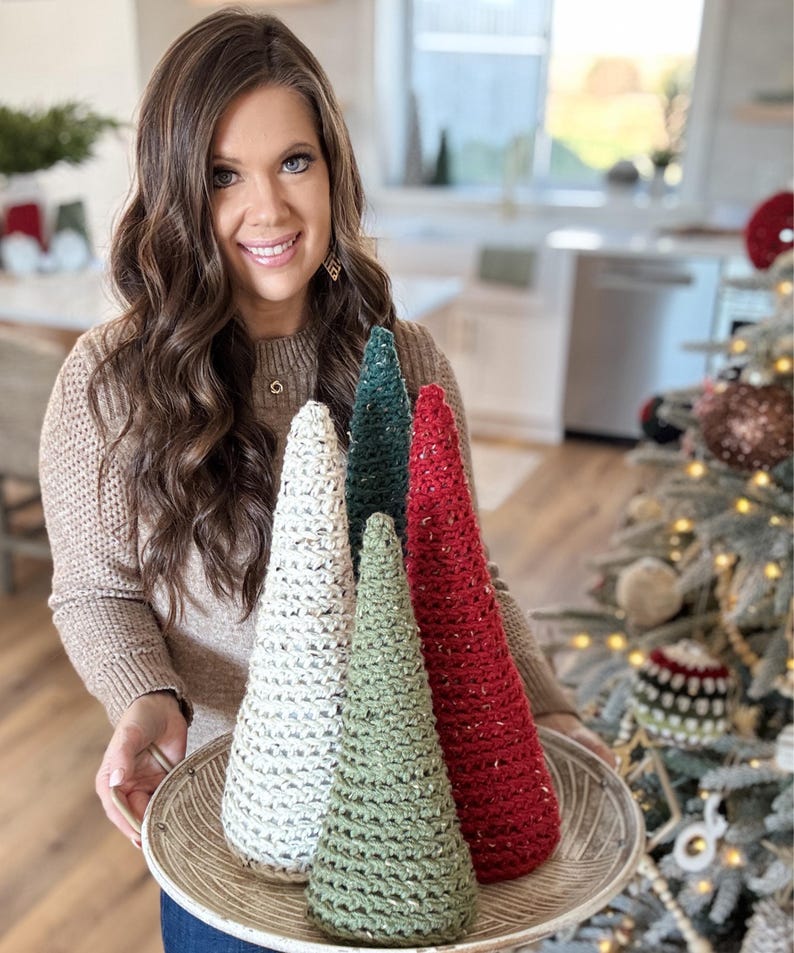May include: Four crocheted Christmas trees in white, green, and red on a silver tray. The trees are cone-shaped and have a sparkly texture.