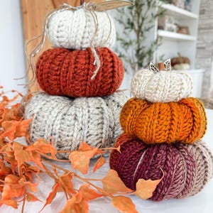 K&ouml;nnte beinhalten: Gestapelte, handgestrickte K&uuml;rbisse in Creme, Orange, Rost und Burgunderrot. Jeder K&uuml;rbis hat einen Stiel und ist Teil einer herbstlichen Dekoration.