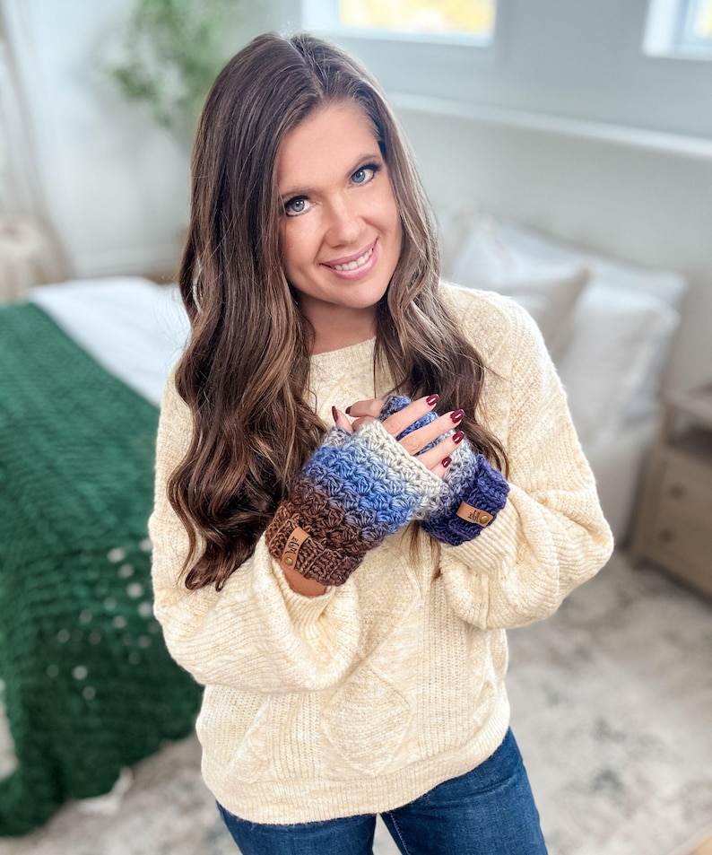 Peut inclure: Mitaines sans doigts crochet&eacute;es dans les tons de marron, bleu et gris. Les gants ont un motif textur&eacute; et de petites &eacute;tiquettes en cuir. La personne porte un pull cr&egrave;me et un jean bleu.