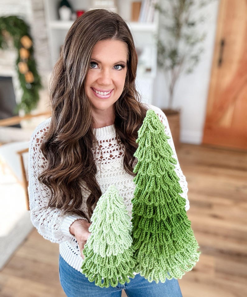 May include: Two handmade crochet Christmas trees in varying shades of green. The trees have a textured, layered design, resembling a fir tree. The larger tree is a vibrant green, while the smaller one is a lighter shade. The trees are displayed against a neutral background.