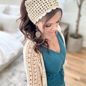 May include: A cream-coloured crochet head wrap with a scalloped edge. The head wrap is paired with a matching crochet cardigan and a teal-coloured crochet top. The outfit is a bohemian style, perfect for a casual, yet stylish look.