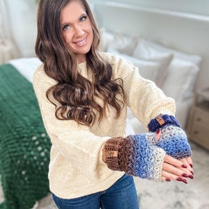 Peut inclure: Mitaines sans doigts crochet&eacute;es dans les tons de marron, bleu et gris. Les gants ont un motif de point textur&eacute; et une petite &eacute;tiquette en cuir. La personne porte un pull cr&egrave;me et un jean bleu.