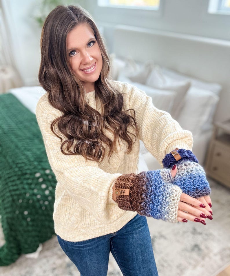 Peut inclure: Mitaines sans doigts crochet&eacute;es dans les tons de marron, bleu et gris. Les gants ont un motif de point textur&eacute; et une petite &eacute;tiquette en cuir. La personne porte un pull cr&egrave;me et un jean bleu.
