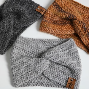 May include: Three knitted headbands in different colors and patterns. The headbands are gray, brown, and gray with a brown stripe. Each headband has a brown leather tag with a logo.