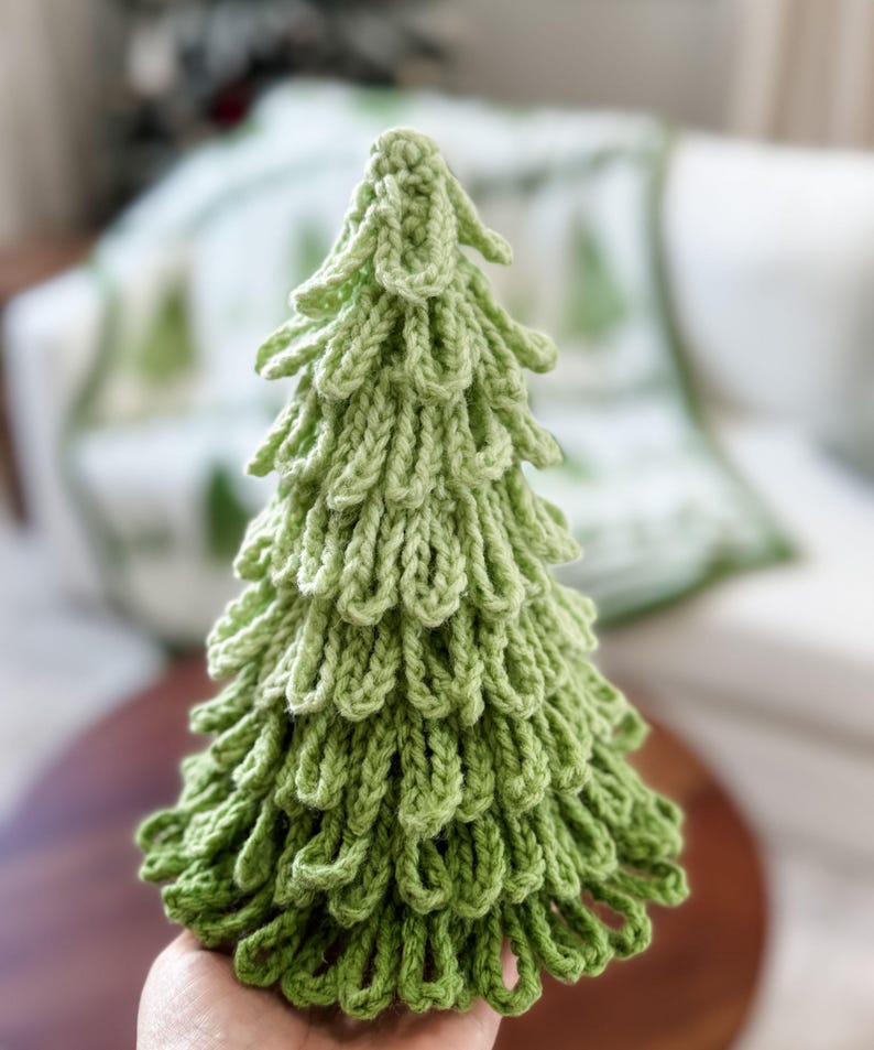 May include: A handmade, green knitted Christmas tree. The tree is a light green color and has a textured, looped design. The tree is a decorative item, perfect for holiday decor.