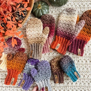 Peut inclure: Une collection de mitaines crochet&eacute;es &agrave; la main, aux couleurs vari&eacute;es : beige, orange, violet et turquoise. Chaque mitaine pr&eacute;sente un poignet c&ocirc;tel&eacute; et une petite &eacute;tiquette en cuir. Les mitaines sont dispos&eacute;es sur une surface textur&eacute;e de couleur cr&egrave;me.