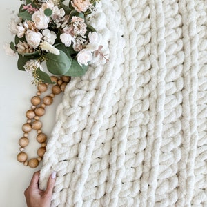 Peut inclure: Une couverture en tricot blanc &eacute;pais avec une texture douce et moelleuse. La couverture est faite de fil &eacute;pais et pr&eacute;sente un motif de tricot torsad&eacute;.