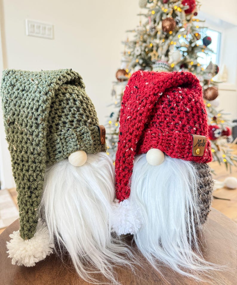 May include: Two crocheted gnomes, one with a green hat and the other with a red hat. Both gnomes have white beards and pom-poms on their hats.