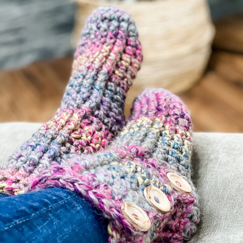 May include: A pair of crocheted slippers with a colourful, multi-coloured pattern. The slippers have wooden buttons on the top.