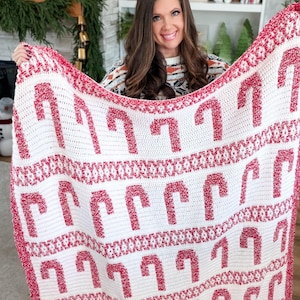 K&ouml;nnte beinhalten: Eine wei&szlig;-rote H&auml;keldecke mit einem sich wiederholenden Muster aus Zuckerstangen. Die Decke hat einen roten Rand und wird pr&auml;sentiert, um das festliche Design hervorzuheben. Diese handgefertigte Decke ist ideal f&uuml;r die Weihnachtszeit.