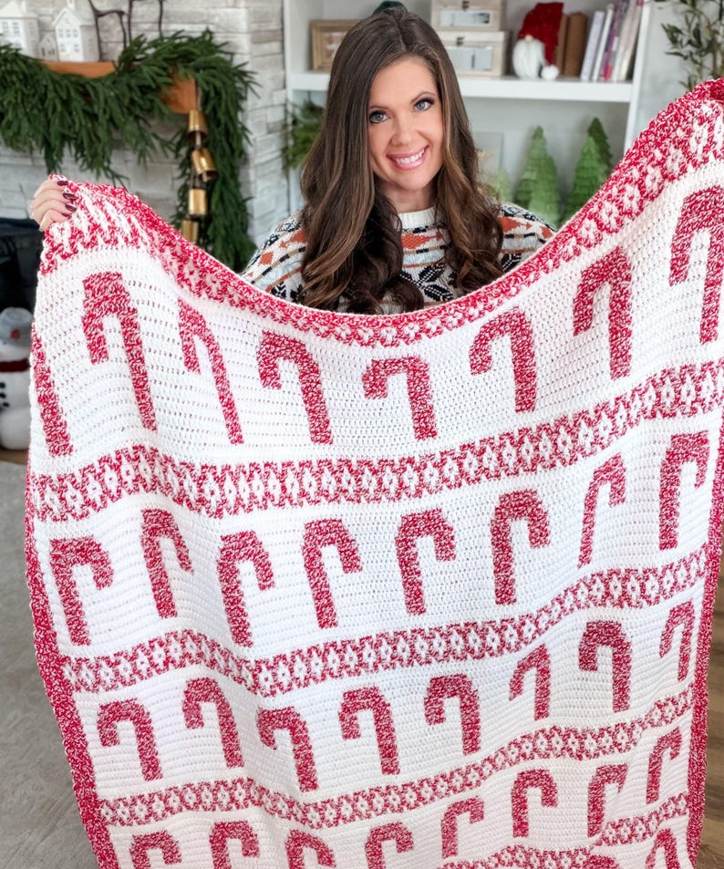 K&ouml;nnte beinhalten: Eine wei&szlig;-rote H&auml;keldecke mit einem sich wiederholenden Muster aus Zuckerstangen. Die Decke hat einen roten Rand und wird pr&auml;sentiert, um das festliche Design hervorzuheben. Diese handgefertigte Decke ist ideal f&uuml;r die Weihnachtszeit.