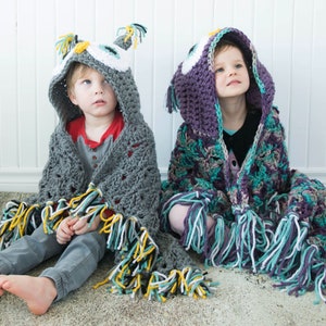 May include: Two children wearing crocheted owl hooded blankets. The blanket on the left is gray with yellow, white, and black fringe. The blanket on the right is purple, teal, and white with white fringe.