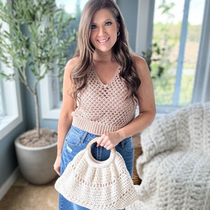 May include: A woman wearing a brown crochet top and a denim skirt is holding a white crocheted bag with a wooden handle.