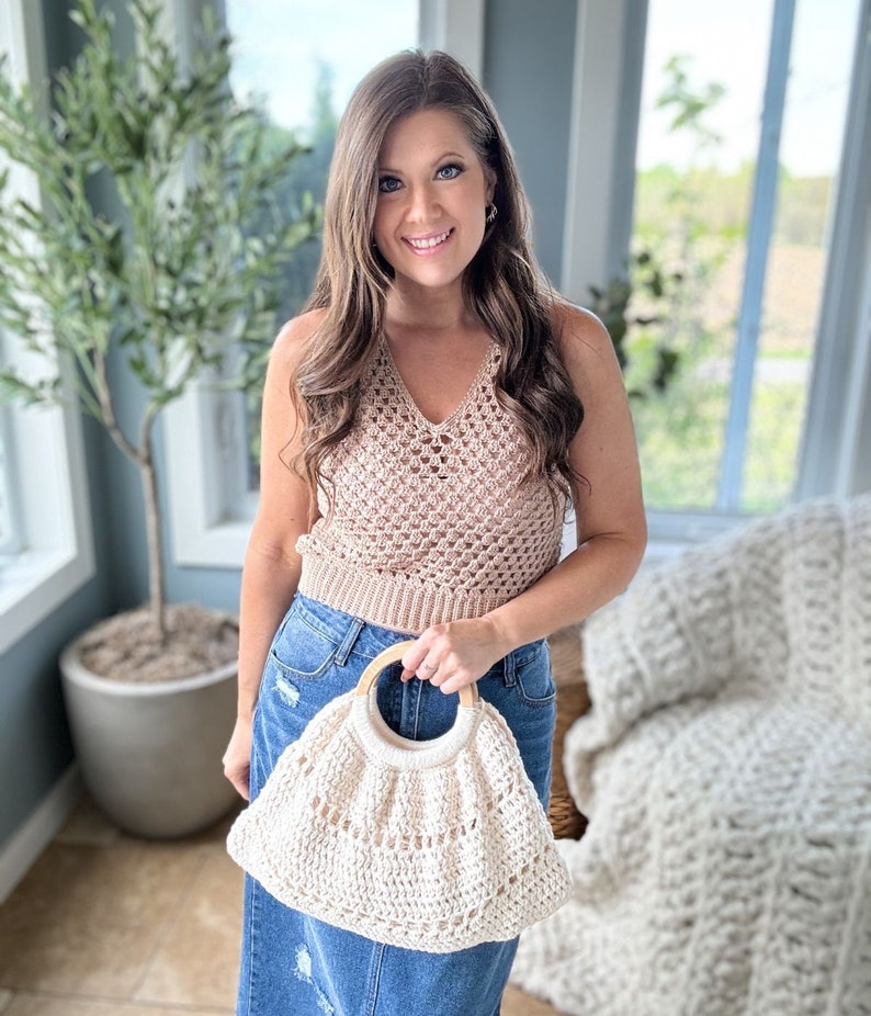 May include: A woman wearing a brown crochet top and a denim skirt is holding a white crocheted bag with a wooden handle.