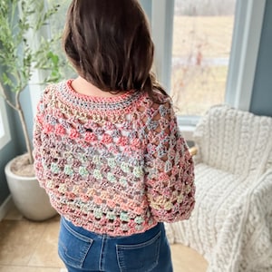 May include: A colorful crochet top with a loose, open-weave design. The top is made with a variety of shades of pink, blue, green, and beige yarn.