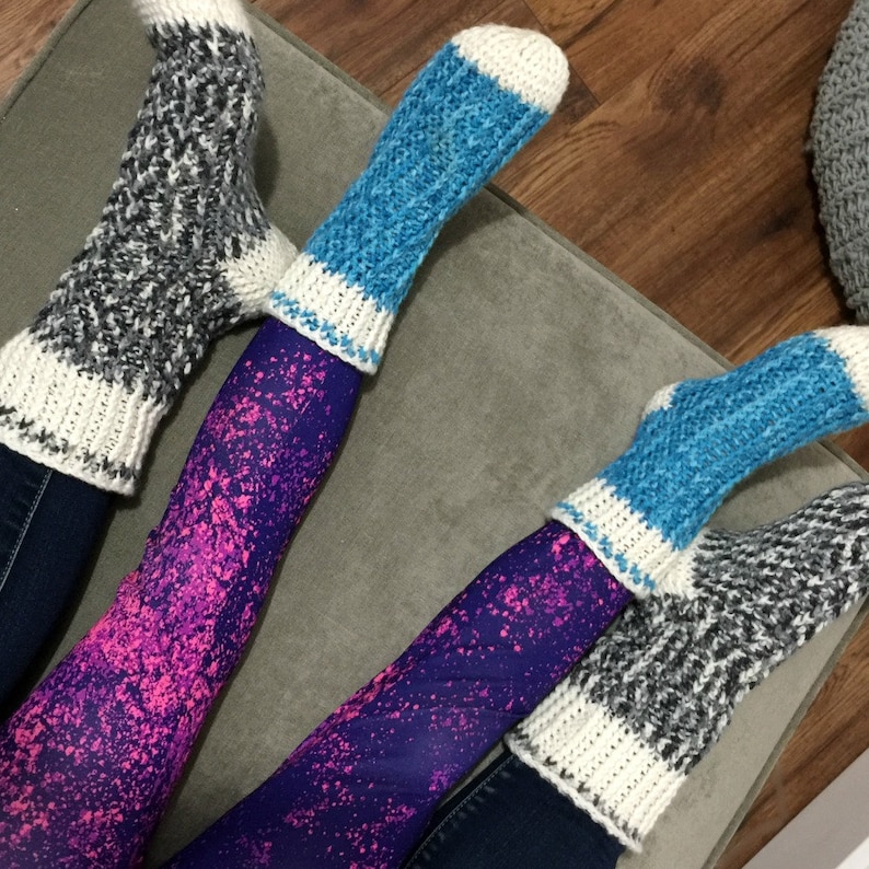 May include: Three pairs of knitted socks in various colors, including white, gray, blue, and pink. The socks are laid out on a gray surface with the toes pointing towards the camera.