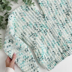 May include: A white crocheted sweater with a speckled pattern of light blue and green yarn.