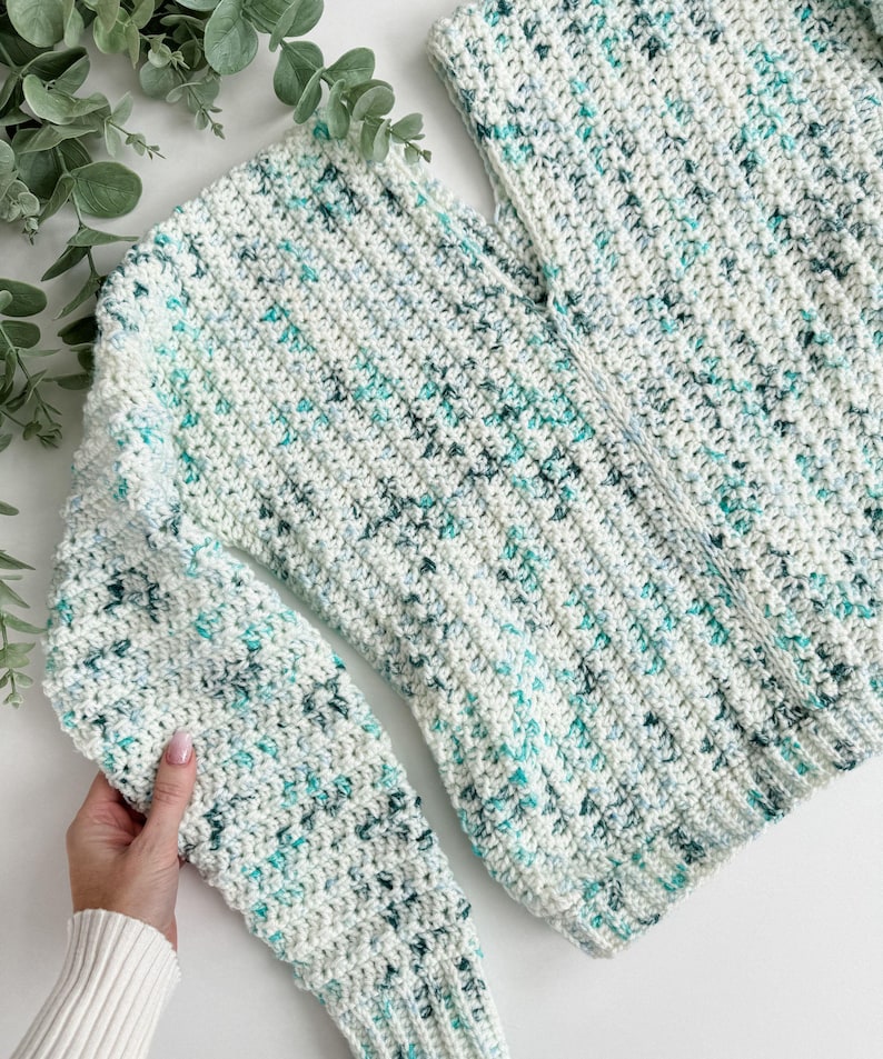 May include: A white crocheted sweater with a speckled pattern of light blue and green yarn.