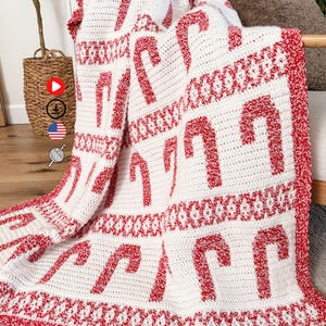 K&ouml;nnte beinhalten: Eine wei&szlig;-rote H&auml;keldecke mit einem sich wiederholenden Zuckerstangenmuster. Die Decke hat einen roten Rand und dekorative N&auml;hte. Das Zuckerstangen-Design ist ein festliches Urlaubsthema.