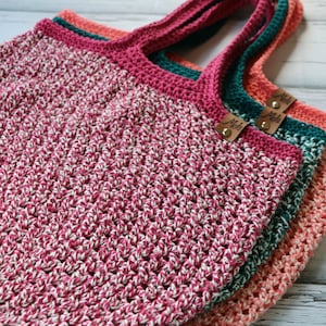 May include: Three crocheted tote bags in pink, teal and orange with a white fleck. Each bag has a brown leather tag with the text "Mel's" on it.