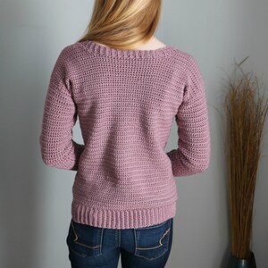 Puede incluir: Un su&eacute;ter de punto de color malva con mangas largas y cuello redondo.