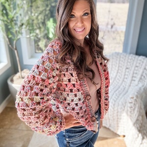 May include: A crocheted cardigan with a colorful, multi-colored pattern. The cardigan has a button closure and long sleeves.
