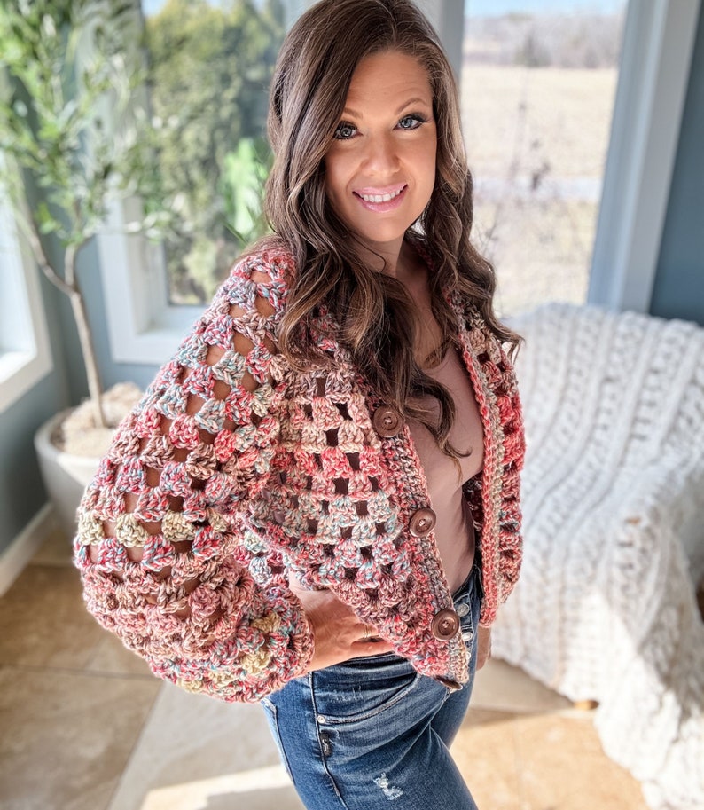May include: A crocheted cardigan with a colorful, multi-colored pattern. The cardigan has a button closure and long sleeves.