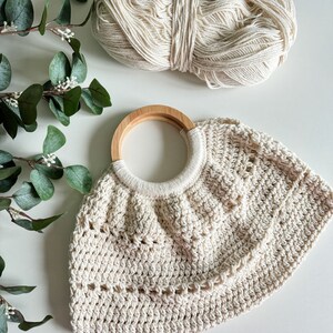 May include: A crocheted cream-colored tote bag with a wooden handle. The bag has a scalloped edge and a delicate openwork pattern.