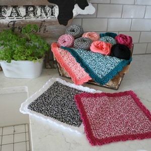 May include: Three crocheted dishcloths in black and white, pink and white, and teal and white. The dishcloths are in a wire basket with balls of yarn in various colors.