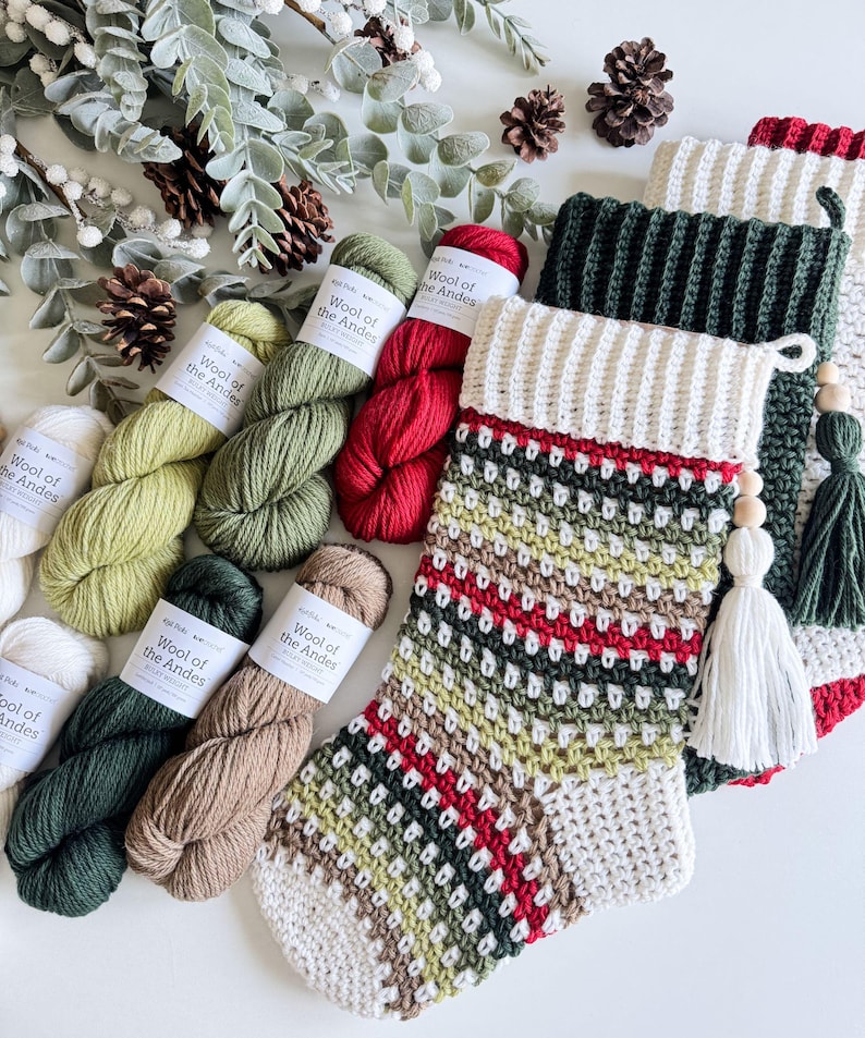 May include: A selection of Christmas stockings and yarn skeins in various colours. The stockings are hand-crocheted with white, green, red, and brown yarn. The yarn skeins are labelled "Wool of the Andes" and are in shades of white, green, and red.