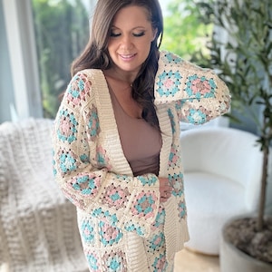 May include: A crocheted cardigan featuring a granny square design in cream, pink and blue hues. The cardigan has a long, open front and bell sleeves.
