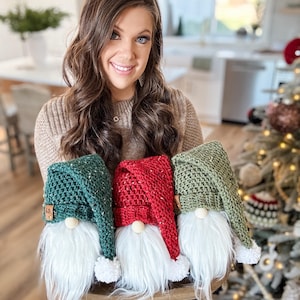 May include: Three crocheted gnomes with white fur beards. The gnomes are wearing green, red, and green hats with white pom-poms.