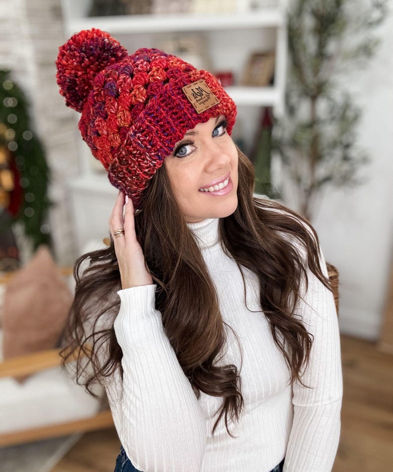 May include: A red, orange, and purple crocheted beanie with a pom pom on top. The beanie has a brown leather patch with the text "Ash & Arrow" on it.