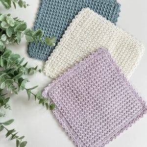 May include: Three crocheted dishcloths in different colors: light blue, cream, and lavender. Each dishcloth has a scalloped edge.