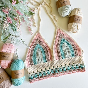 May include: A crocheted halter top with a rainbow pattern in shades of pink, green, and beige. The top has a scalloped hem and is made with a sport weight yarn.