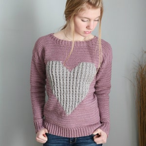 Puede incluir: Un su&eacute;ter de punto de color malva con un dise&ntilde;o de coraz&oacute;n de punto gris.