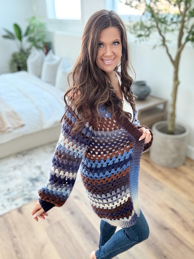K&ouml;nnte beinhalten: Ein lang&auml;rmliger, geh&auml;kelter Cardigan mit einem gestreiften Muster in Braun-, Blau- und Wei&szlig;t&ouml;nen. Der Cardigan hat eine lockere Passform und einen entspannten Stil.