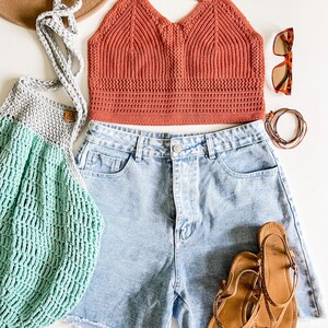 May include: A light blue denim shorts with a crocheted orange top and a green crocheted bag.