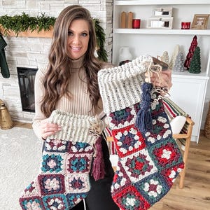 Puede incluir: Dos calcetines de Navidad tejidos a crochet con un patrón de cuadrados de la abuela en tonos de rojo, verde, azul, blanco y rosa. Los calcetines tienen un puño de crochet blanco y una borla burdeos.