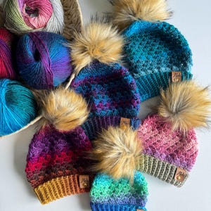 May include: Five colourful crocheted hats with faux fur pom poms. Each hat has a different colour gradient and a small leather tag with the word "Mids" on it.