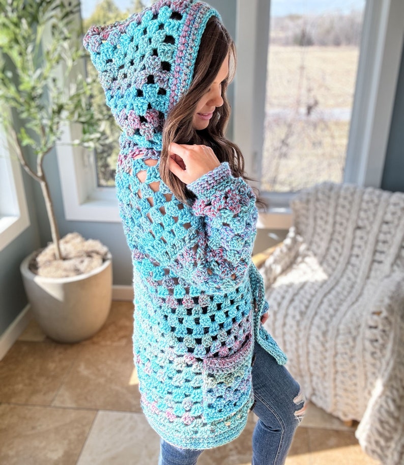 May include: A light blue crochet cardigan with a hood and a pocket. The cardigan is made with a variegated yarn that has shades of blue, pink, and purple.