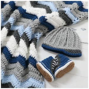May include: A crocheted baby blanket with a chevron pattern in shades of blue, grey, and white. The blanket is paired with a grey crocheted hat and a pair of blue crocheted baby shoes.