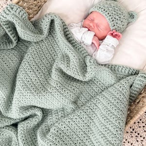 Puede incluir: Una manta de beb&eacute; tejida a ganchillo en color verde salvia con un patr&oacute;n de punto de estrella texturizado, junto con un gorro de beb&eacute; a juego en verde salvia con peque&ntilde;as orejas redondeadas. El conjunto est&aacute; hecho de hilo y es uniforme.