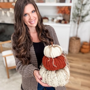 K&ouml;nnte beinhalten: Ein Stapel von drei handgefertigten H&auml;kelk&uuml;rbissen in Creme, Orange und Beige. Jeder K&uuml;rbis hat einen Stiel und ist mit Bindfaden gebunden. Die K&uuml;rbisse sind eine herbstliche Dekoration.
