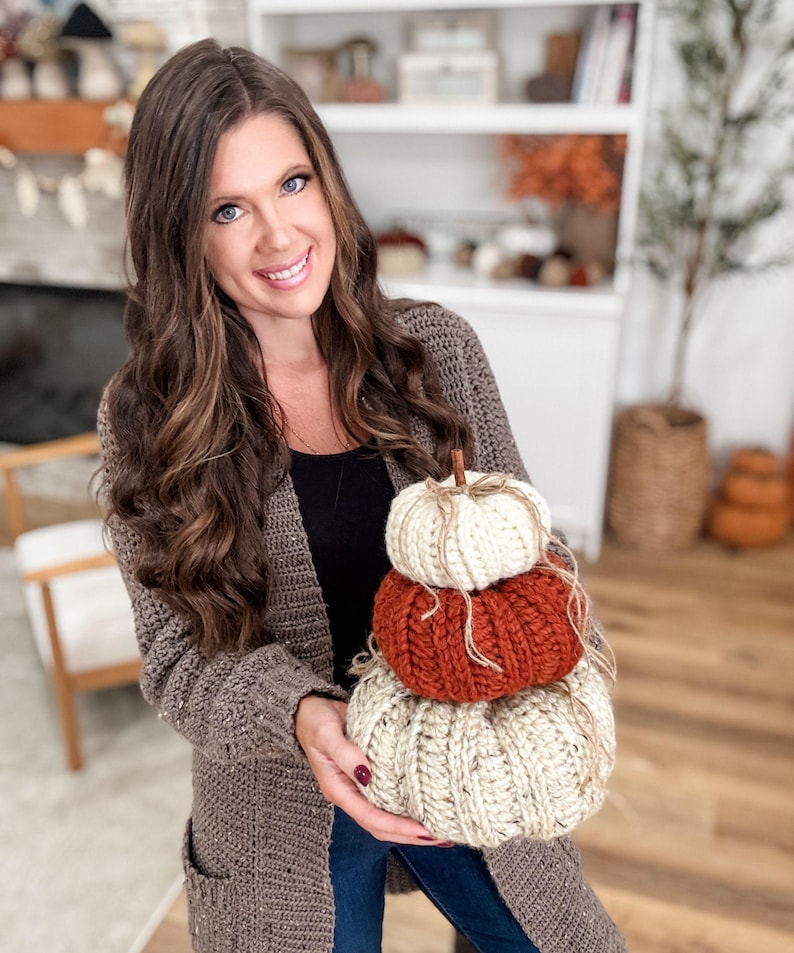 K&ouml;nnte beinhalten: Ein Stapel von drei handgefertigten H&auml;kelk&uuml;rbissen in Creme, Orange und Beige. Jeder K&uuml;rbis hat einen Stiel und ist mit Bindfaden gebunden. Die K&uuml;rbisse sind eine herbstliche Dekoration.